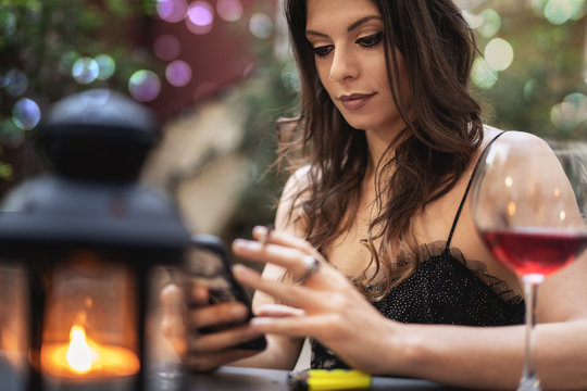 Beautiful Woman Using Smart Phone On A Restaurant Table While Drinking A Glass Of Red Wine