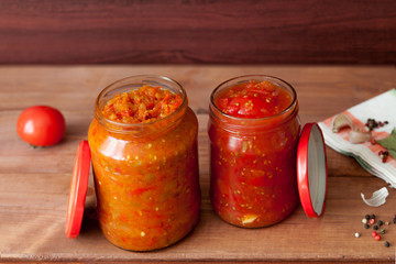 Homemade prepared two fermented vegetable glass jars with carrot, red tomatoes and salsa with spice on rustic wooden background.