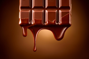 Chocolate bar with melted dark chocolate dripping over dark brown background. Confectionery concept...
