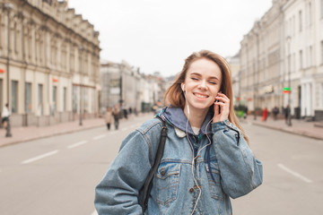 Portrait of a smiling girl in the casual clothing listens to music in the headphones with her eyes closed, gets a posterity. A happy girl listens to music at a walk, wearing a jeans jacket.