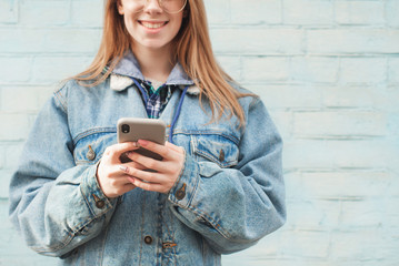 Close up photo, stylish hipster girl uses a smartphone on the background of a blue wall, hands with a smartphone close-up, wearing a jeans jacket. Copyspace