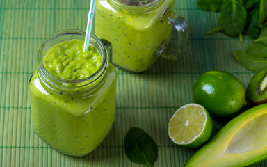 Green smoothie in glass on green background made by avocado, lemon and kiwi.