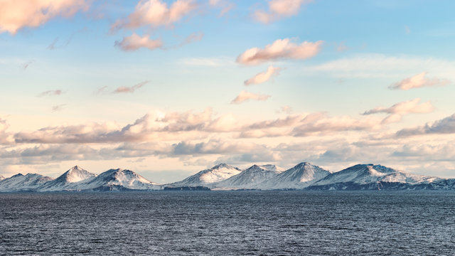 Snow peaks, glaciers and rocks of Aleutian islands in sunny winter day as viewed from ship passing in calm sea