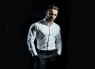 Fototapeta na wymiar Handsome man standing with arms in pockets isolated on a black background. A handsome confident young man standing and smiling in a white shirt. Portrait of young man