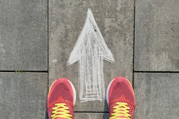 Arrow sign painted on gray sidewalk with women legs in sneakers, top view