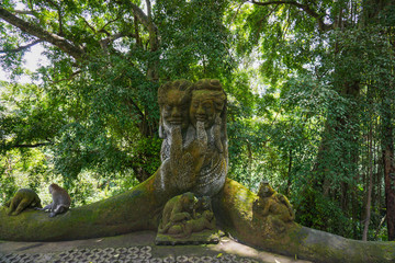 Monkey sitting on a stone sculpture at sacred monkey forest in Ubud, island Bali, Indonesia