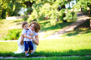 Fototapeta premium Mom hugs little son and playing in park at sunset time. People having fun on forest. Concept of friendly family and of summer vacation.