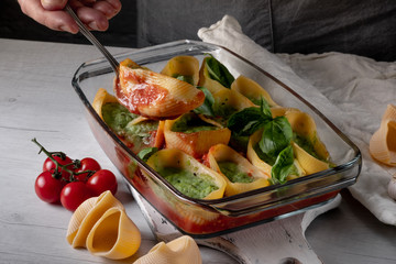 Vegetarian pasta recipe cooking with ingredients - basil, herbs, garlic, tomatoes and cheese, baking in glass tray on white wooden background. Top view, flat lay.