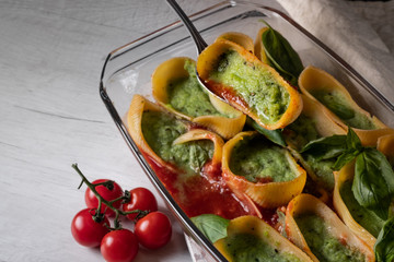 Pasta recipe cooking with ingredients - basil, herbs, garlic, tomatoes and cheese, baking in glass tray on white wooden background. Top view, flat lay.