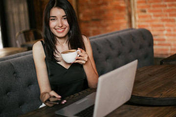 Business woman working on a laptop, using phone and drinking coffee in a cafe.