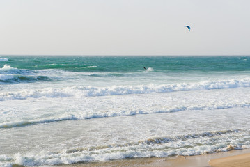 Unrecognisable man with parachute rides on a surfboard on large waves in the sea or ocean.