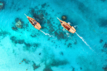 Fototapeta na wymiar Aerial view of the fishing boats in clear blue water at sunset in summer. Top view from drone of boat, sandy beach. Indian ocean. Travel in Zanzibar, Africa. Landscape with sailboats, sea. Seascape