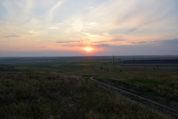 Fototapeta premium Republic of Moldova fields landscape. Countryside sunset with dirty road between fields in Moldova.