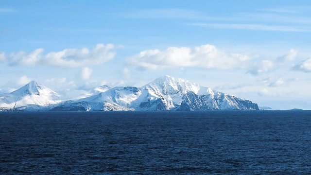 Snow peaks, glaciers and rocks of Aleutian islands in sunny winter day as viewed from ship passing in calm sea