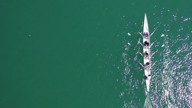 Aerial drone bird's eye top view video of sport canoe operated by team of young men and women in open ocean sea