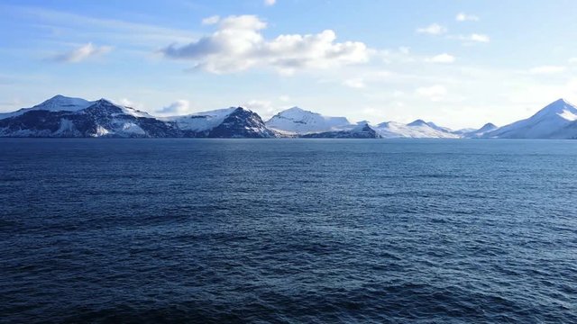 Snow peaks, glaciers and rocks of Aleutian islands in sunny winter day as viewed from ship passing in calm sea