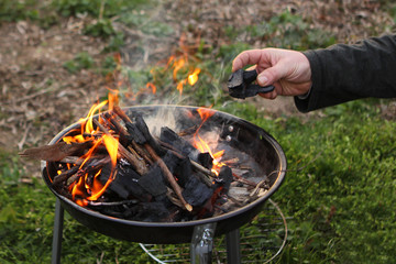 Hand puts coals into a burning fire in a compact grill, nature