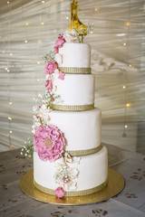 Wedding cake with white and pink icing flowers and golden cake topper