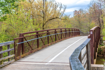 A rusty steel and concrete bridge on a treated lumber fitness trail in the spring forest