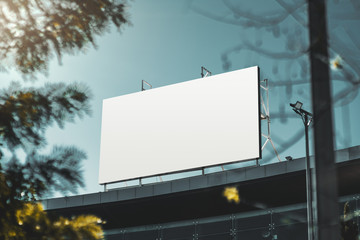An empty huge poster mockup on the roof of a mall; white template placeholder of an advertising billboard on the rooftop of a modern building framed by trees; blank mock-up of an outdoor info banner - obrazy, fototapety, plakaty