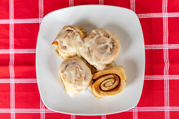 Home Made Glazed Iced Sugar Cinnamon Rolls on a Square White Plate and a Red Plaid Cloth
