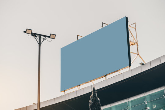 An empty huge poster mockup on the roof of a shopping mall; blue solid template placeholder of an advert billboard on the rooftop of a modern building; blank mock-up of an outdoor information banner