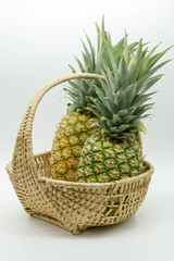 angled photo of two pineapples with large stems in a wicker basket on an isolated white background