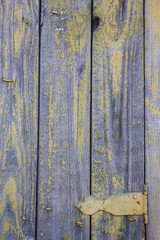 Tekturas wooden fence with remnants of purple and yellow paint and door hinges