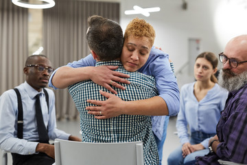 Portrait of mixed race woman hugging psychologist during therapy session in support group, copy...