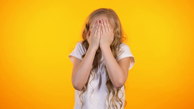 Cute scared schoolgirl closing face with palms, childish fears, unexpected news