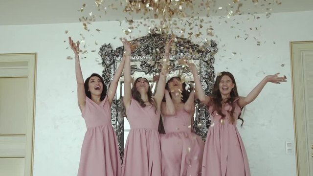 Four happy bridesmaids in evening dress throwing up golden wrappers indoors
