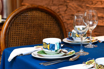 restaurant table with sardine decorated cups and blue tablecloth, elegant dining setup with glassware and cutlery, portuguese culture and gastronomy symbol sardine, stylish table arrangement for meal