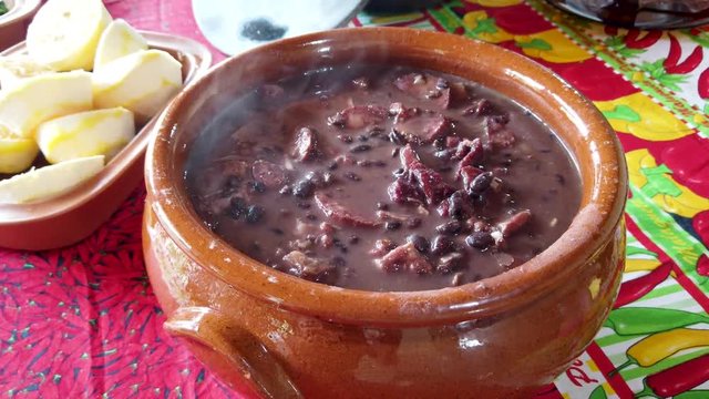 Tradicional brazilian feijoada pan served in a clay pot with smoke, stable  close up