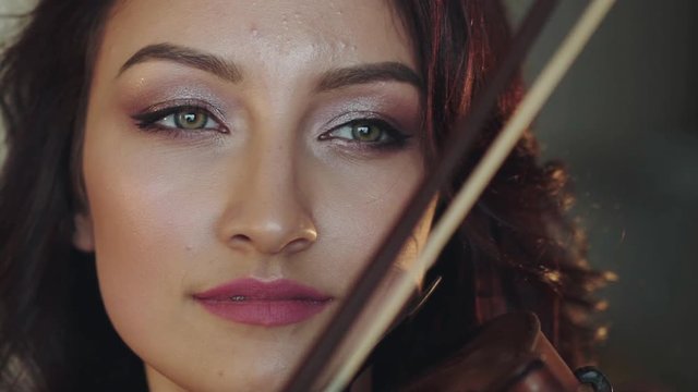 Close portrait of beautiful female violinist swaying the fiddlestick on string