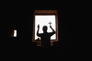 Human praying to the GOD while holding a crucifix symbol in old room