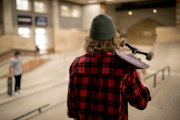 Back view portrait of long haired skater standing in extreme sports park holding skateboard , copy space - Powered by Adobe