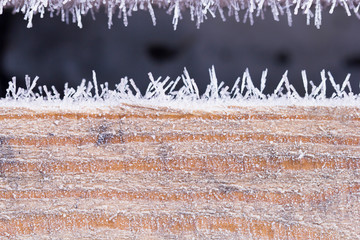The wooden resinous board covered with peaked hoarfrost along the edges. A resinous wooden surface in a beautiful frost. Background from a hoarfrost-covered wooden surface.