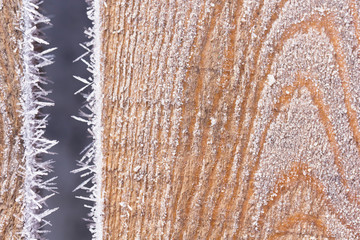 The wooden resinous board covered with peaked hoarfrost along the edges. A resinous wooden surface in a beautiful frost. Background from a hoarfrost-covered wooden surface.