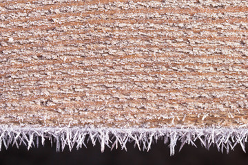 The wooden resinous board covered with peaked hoarfrost along the edges. A resinous wooden surface in a beautiful frost. Background from a hoarfrost-covered wooden surface.