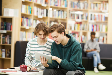 Concentrated thoughtful young students in casual clothing using digital tablet while brainstorming...