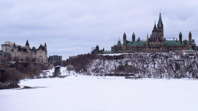 Landscape of Parliament Hill in Ottawa, Ontario, Canada.  The Parliament Building on Canada stands tall on Parliament Hill on a grey gloomy day, with the Ottawa River still frozen from a cold winter.