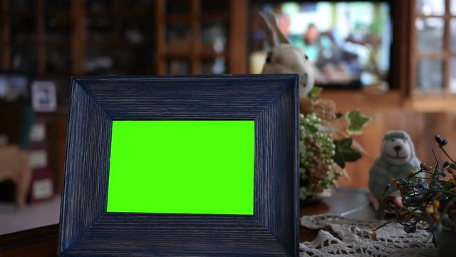 Green screen picture frame sitting on coffee table in foreground with tv in background