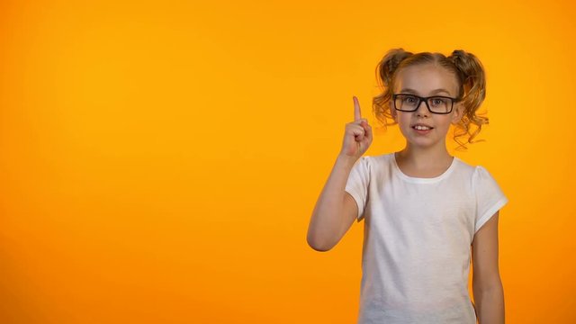 Little genius girl raising finger up isolated on orange background, having idea