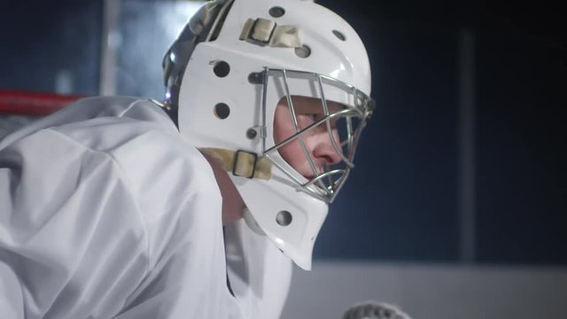 Side view medium shot of concentrated middle-aged ice hockey player in helmet standing near net and thinking