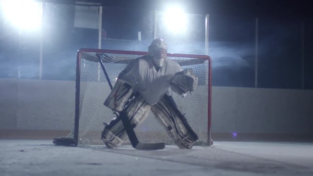 Male ice hockey goaltender standing on rink, holding hockey stick and not letting puck enter the net