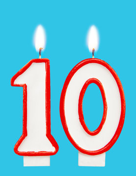 Burning wax candle for a birthday cake in the form of number ten. Blue background