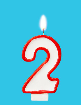 Burning wax candle for a birthday cake in the form of number two. Blue background