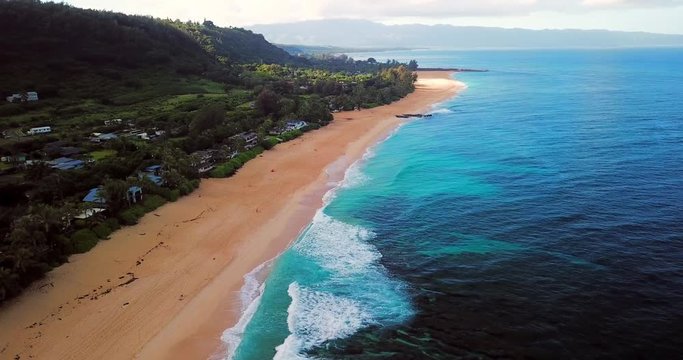 Aerial: Panning Over Ocean, Sandy Beach & Beachfront Buildings & Vegetation in Oahu, Hawaii