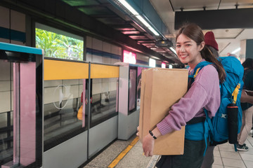 Fototapeta na wymiar Traveler asian woman with backpack carrying souvenir in big paper box in subway station.
