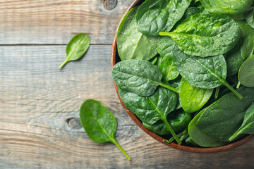 Fresh spinach leaves in bowl on wooden table.